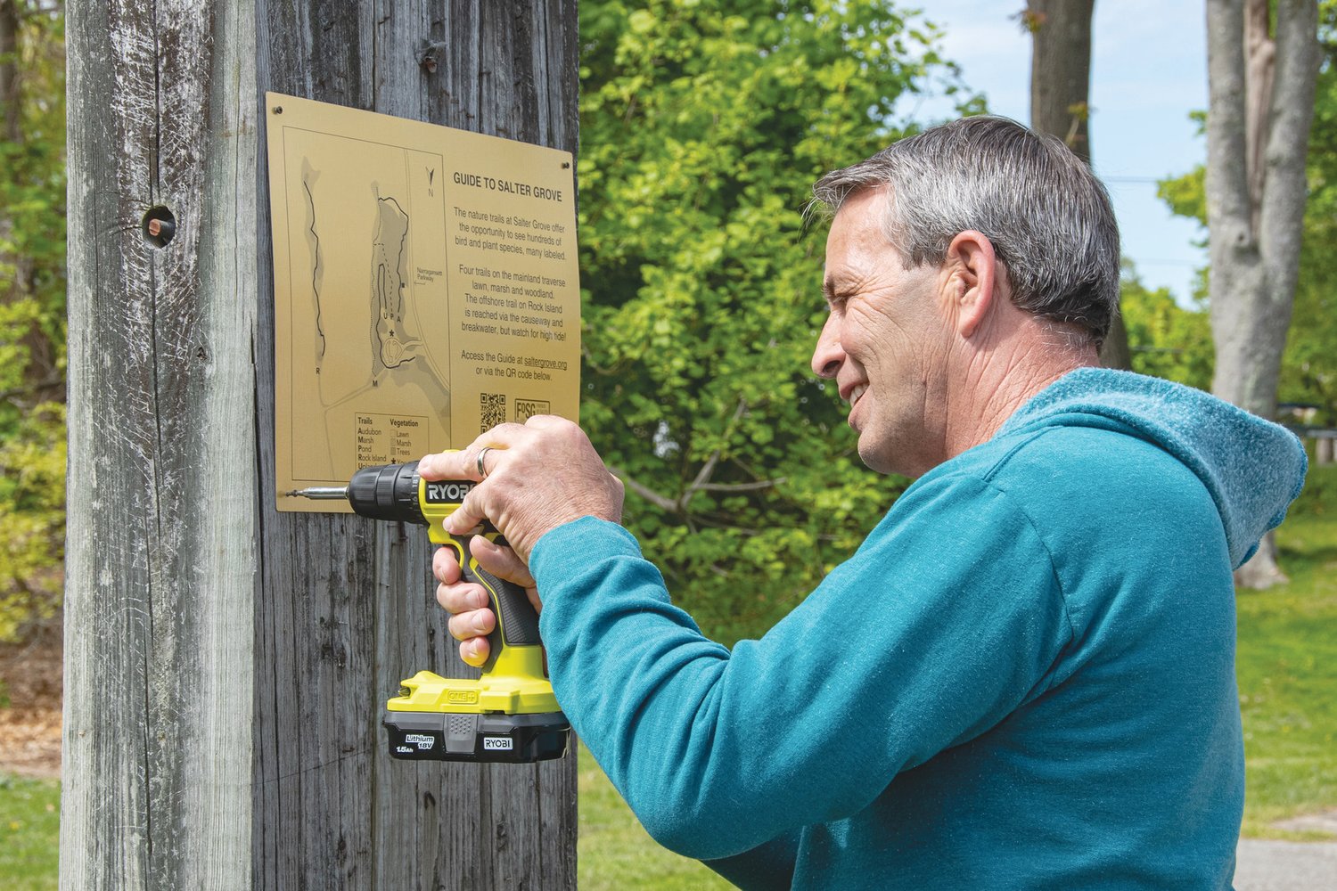 HE KNOWS WHAT HE’S DOING: Mayor Frank Picozzi goes back to his construction days as he helps to attach an orientation sign at the entrance of the park. The sign includes a QR code that will link visitors to the new online guide, as well as a trail map.